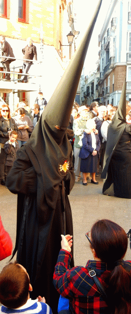 A nazareno reaches into his (or her?) cloak for a holy card for a child on the streets of Cadiz